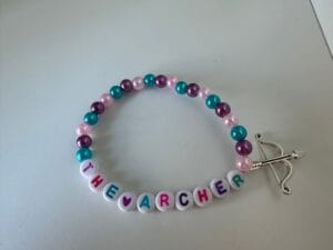 pink, blue and purple taylor swift friendship bracelet with bow and arrow charm and letters spelling 'the archer'
